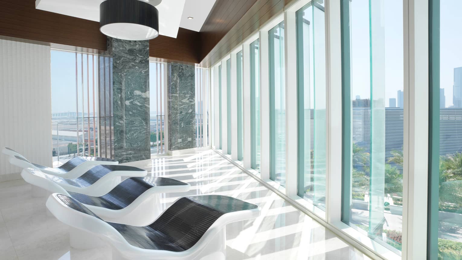 White-and-black recliners in front of floor-to-ceiling glass windows in bright relaxation room