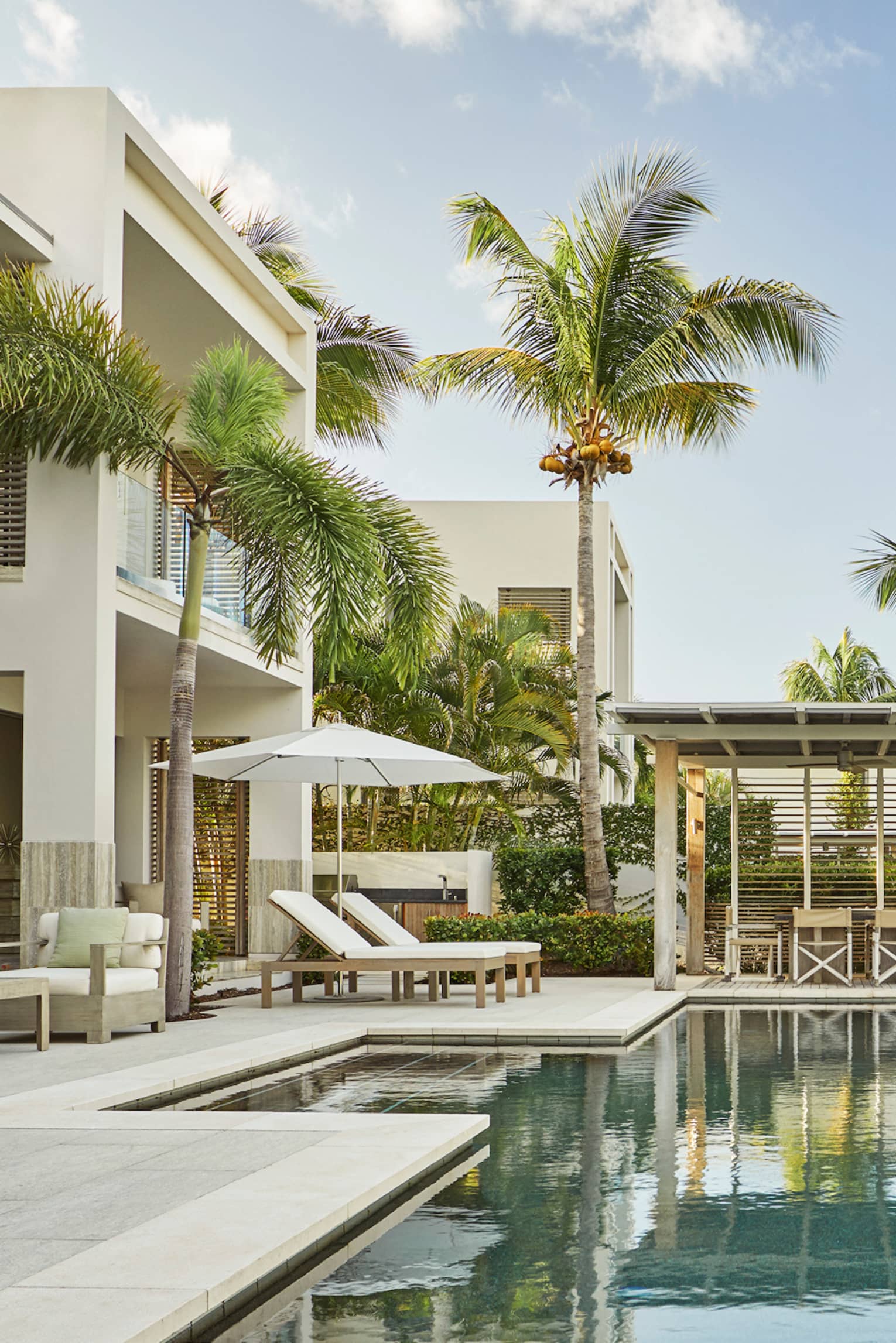 Tall palm trees reflecting on private pool on patio under two storey white villa