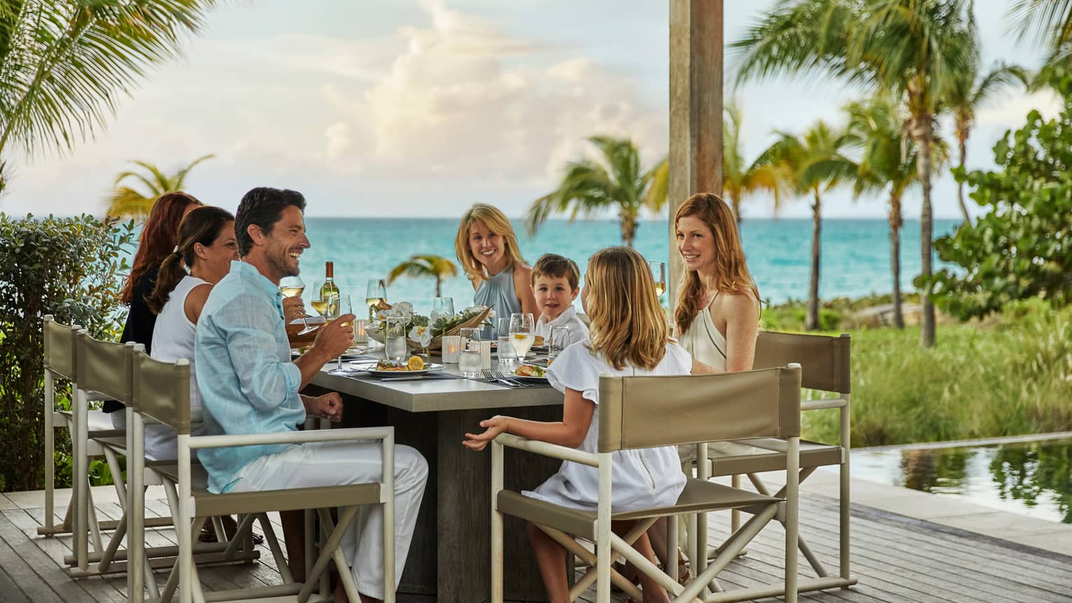 Smiling family dines around patio table, ocean views