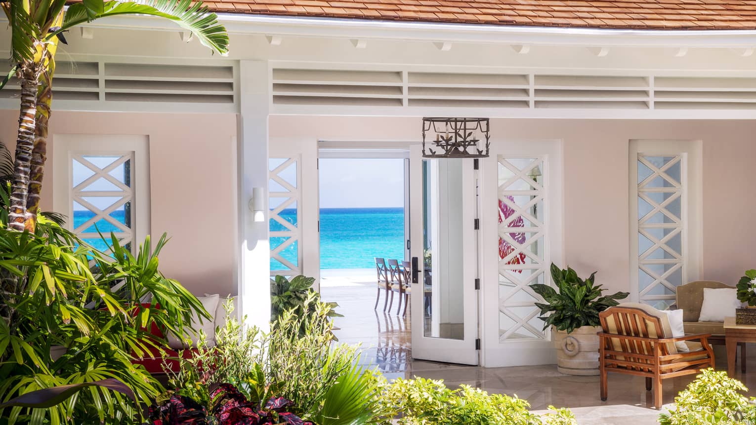 Tropical gardens in front of bright private villa entrance, open door revealing blue ocean in background