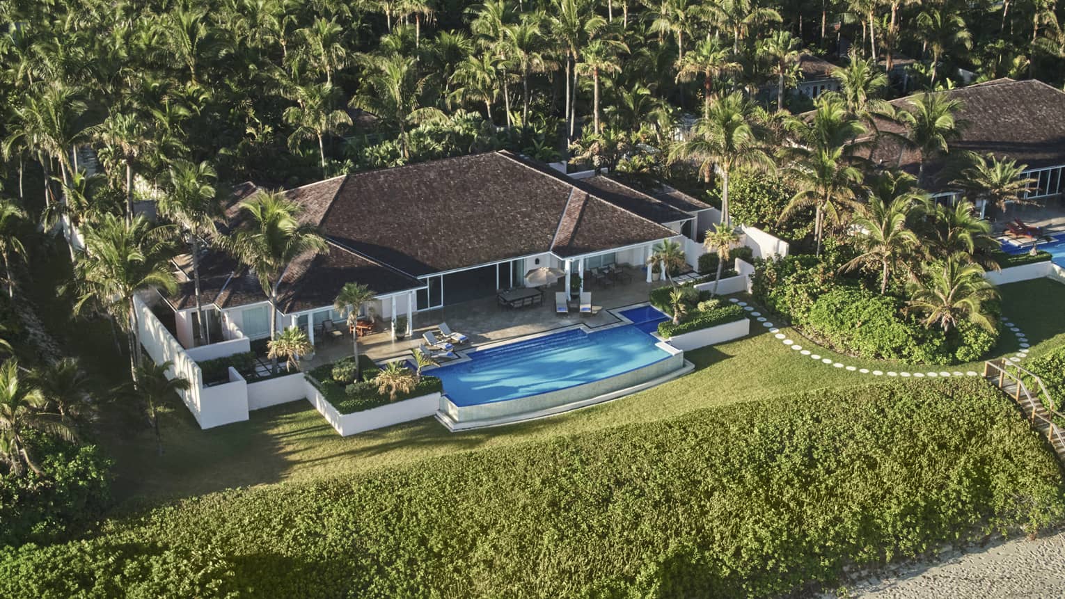 Aerial view of large Four Seasons Ocean Club villa bungalow, pool and lawns behind greenery, sand beach