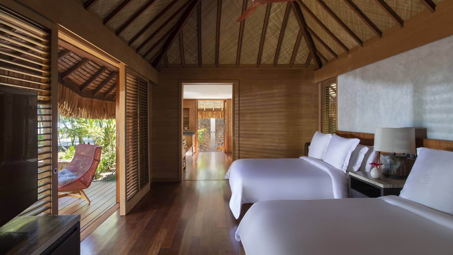 Two queen beds in a villa, with teak floors, a thatched roof and a walk-out patio