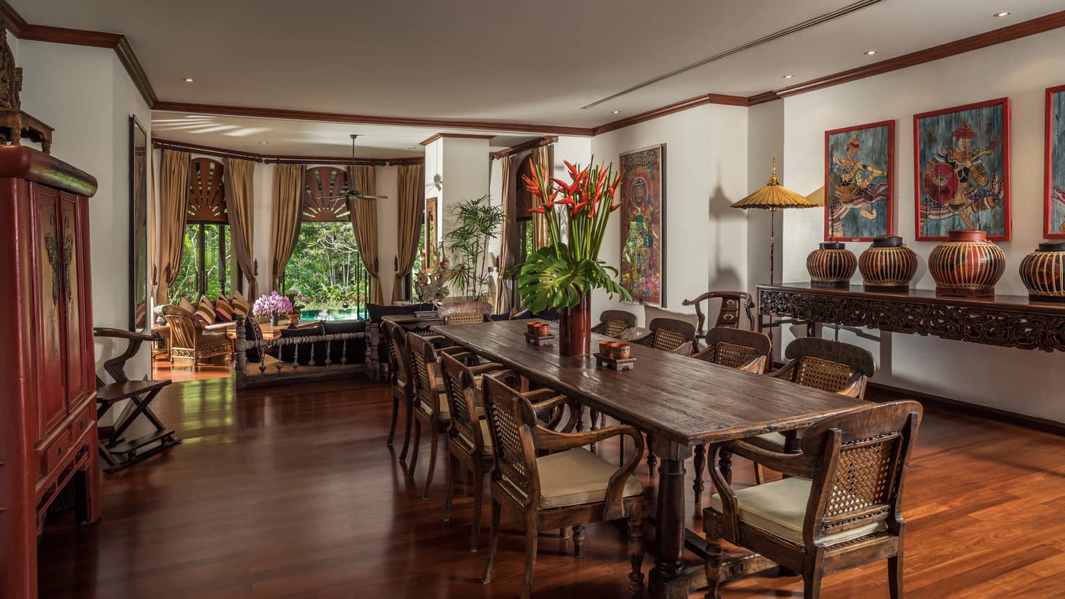 Long wood dining table with vase with tall tropical flowers in bright room