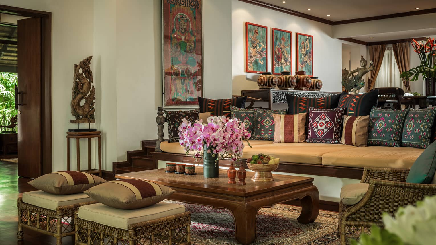Residence living room with long sofa and two ottomans covered with Thailand textile pillows, wood table