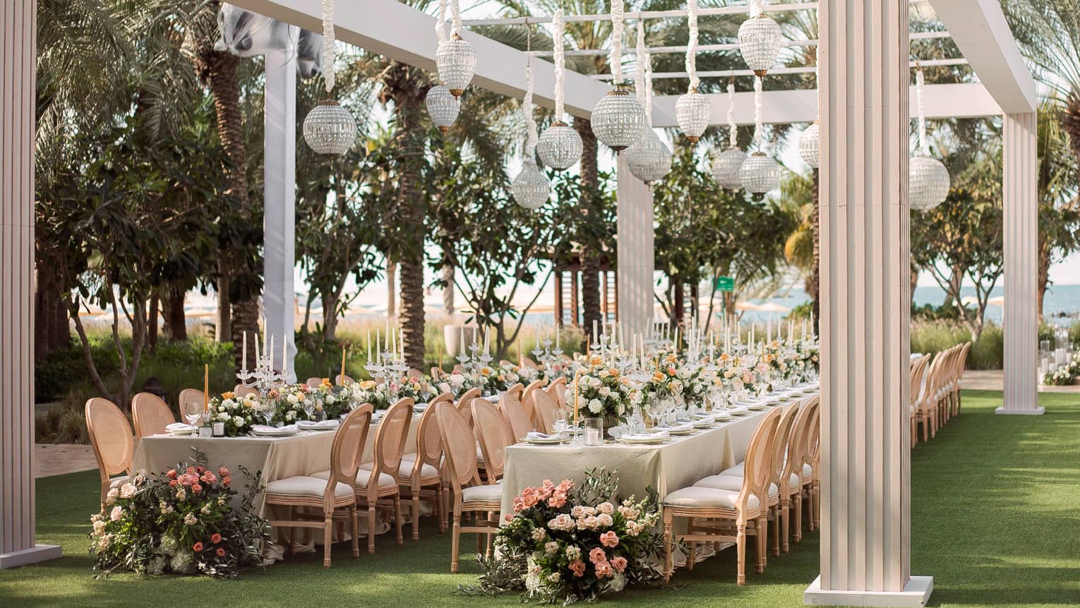 Garden wedding, glass lanterns hang from white pergola over long dining tables
