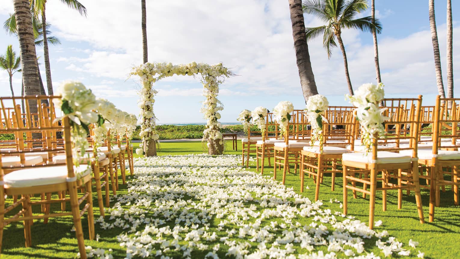Outdoor wedding ceremony set up, white flowers along aisle between rows of chairs, altar