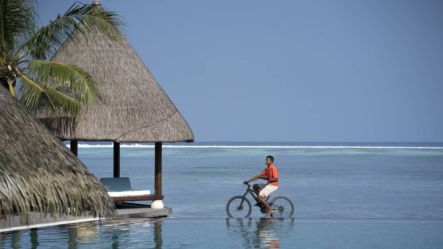 Man riding bicycle in shallow water, view of vast sea behind him