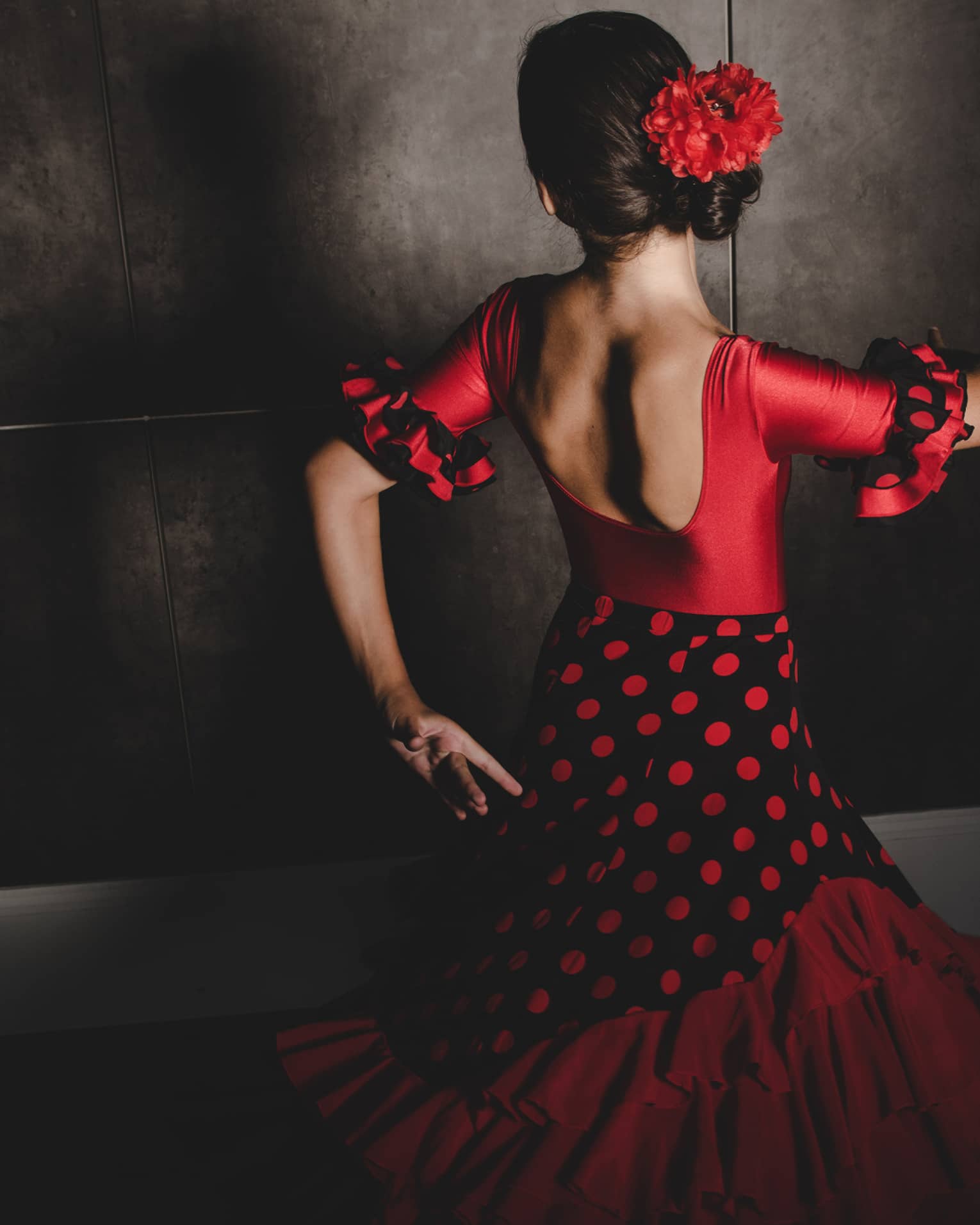 A woman wearing a black and white salsa dancing dress and red flower in her hair dances with her face turned away from the camera 
