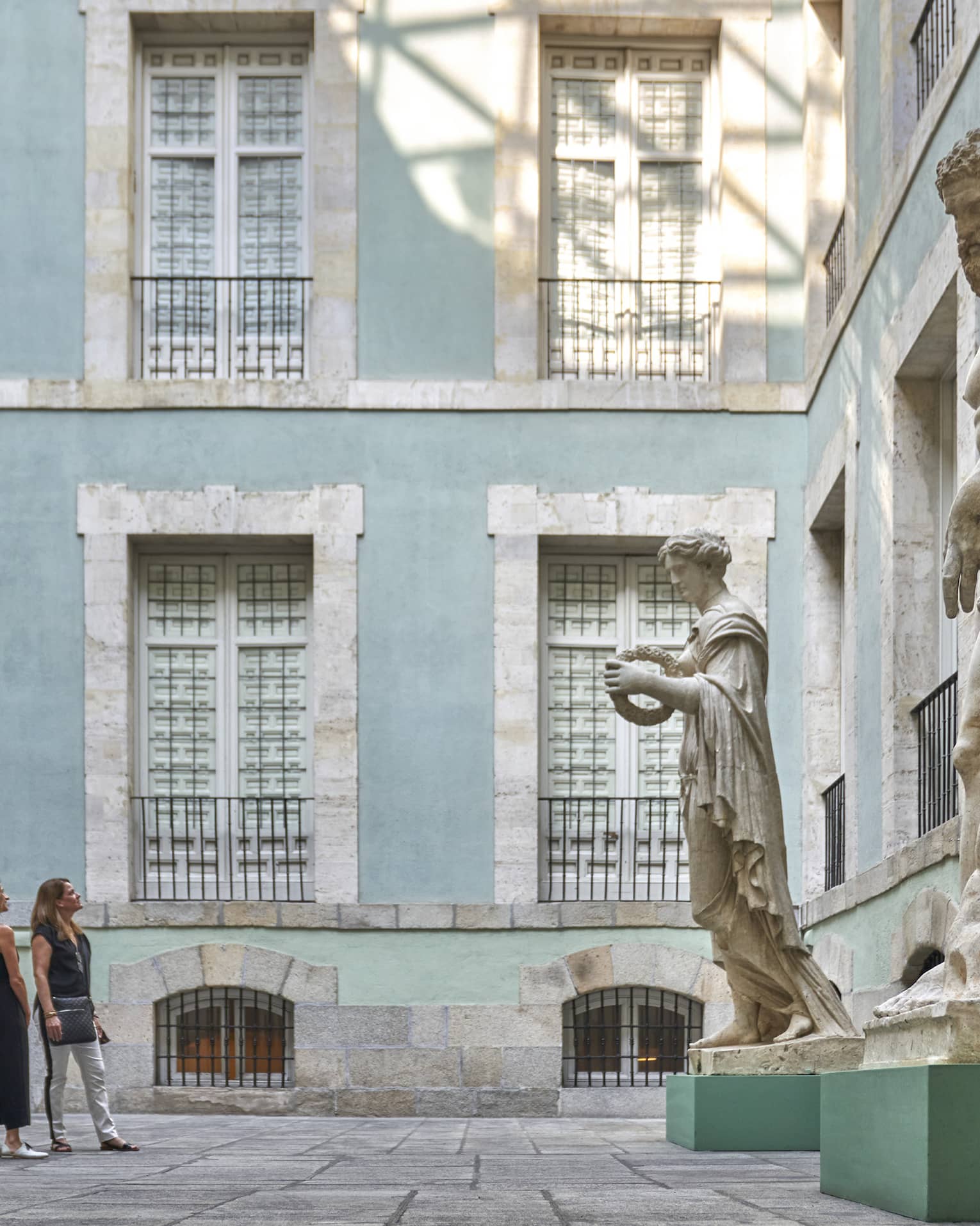 Two women observe large sculptures in a courtyard surrounded by light blue building