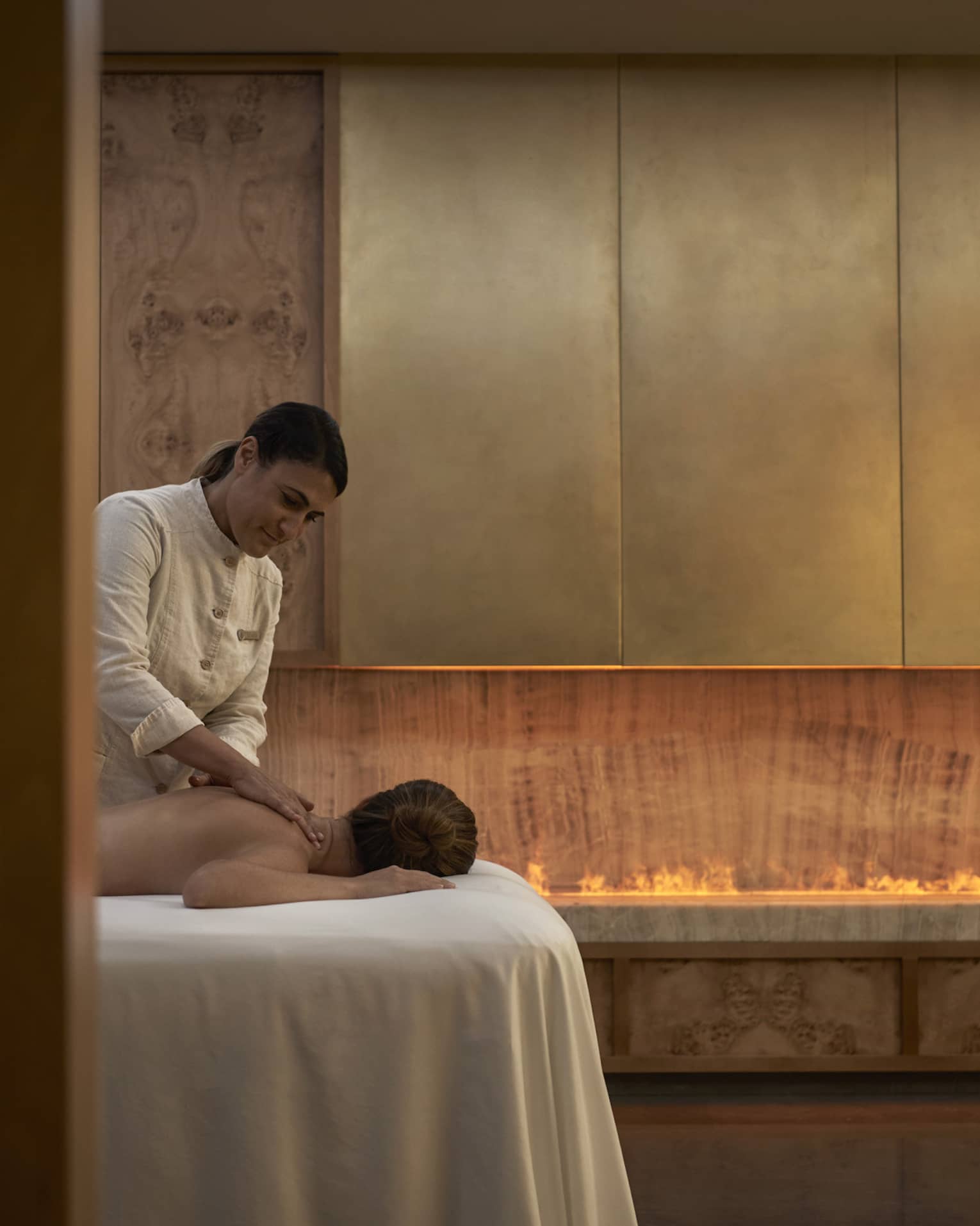 Person facedown on white spa table receiving massage from spa therapist