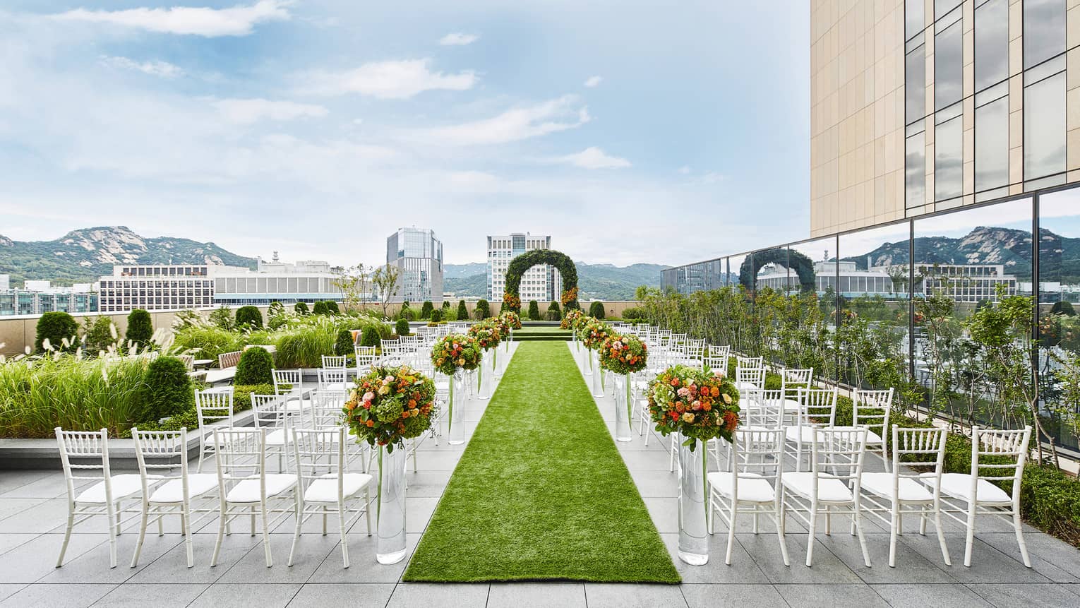 Rooftop patio wedding ceremony set up, rows of white chairs and green aisle facing altar